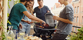 Freunde stehen um einen Griller und grillen