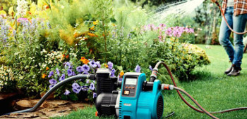 Gartenpumpe im Vordergrund im Hintergrund gie&szlig;t eine Frau