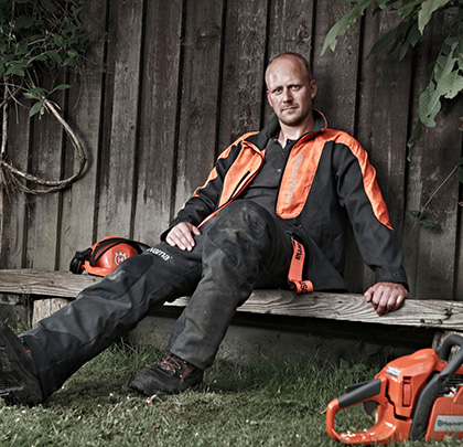 Forstarbeiter sitzt auf einer Bank und trägt einen Forstschutz - Husqvarna.