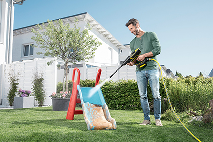 Mann reinigt eine Kinderrutsche mit dem Hochdruckreiniger der Marke Kärcher.