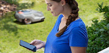Frau steuert den Roboterrasenm&auml;her durch ihr Smartphone.