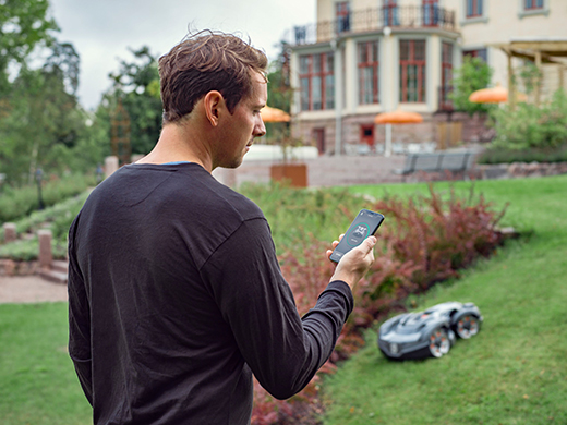 Mann steuert den Mähroboter durch sein Smartphone.