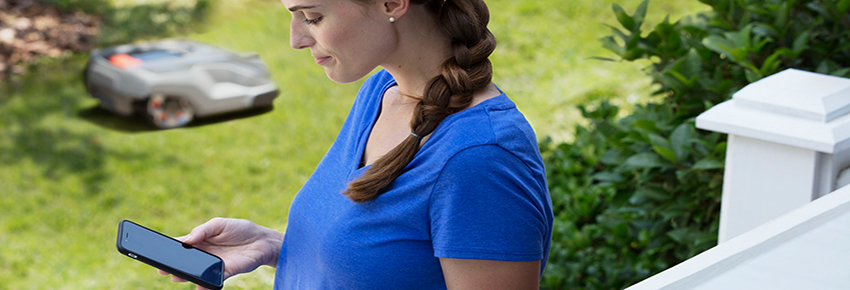 Frau steuert den Roboterrasenm&auml;her durch ihr Smartphone.