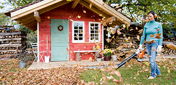 Frau arbeitet mit einem Laubblasger&auml;t im Garten und tr&auml;gt dabei einen Geh&ouml;rschutzb&uuml;gel.