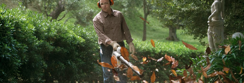 Mann arbeitet mit einem Laubblasger&auml;t und tr&auml;gt dabei einen Geh&ouml;rschutzb&uuml;gel.