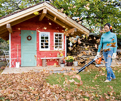 Frau arbeitet mit einem Laubblasgerät im Garten und trägt dabei einen Gehörschutzbügel.
