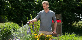 Mann bew&auml;ssert seine Blumen durch einen Schlauch.