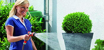 Frau bew&auml;ssert die Pflanzen vor dem Haus mit einem roten Gartenschlauch.