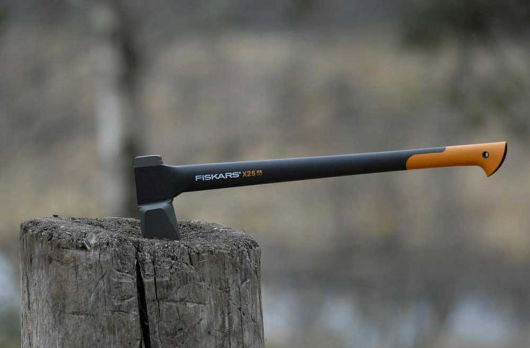 Axt der Marke Fiskars steckt in Baumstamm.