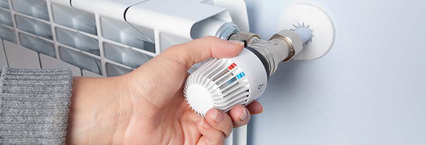 Mensch dreht Heizk&ouml;rper um die Temperatur zu verstellen.