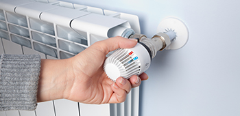 Mensch dreht Heizk&ouml;rper um die Temperatur zu verstellen.