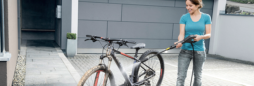 Frau reinigt ihr Fahrrad mit einem schwarzen Hochdruckreiniger.