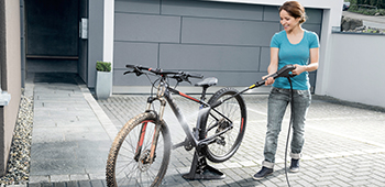 Frau reinigt ihr Fahrrad mit einem schwarzen Hochdruckreiniger.