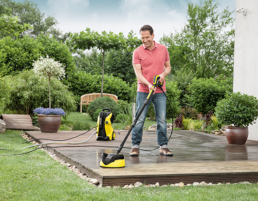 Mann reinigt Holzterasse mit einem Hochdruckreiniger der Marke Kärcher.