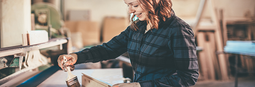 Frau streicht das Holz mit einem Pinsel.