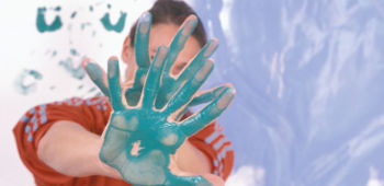 Frau verdeckt ihr Gesicht durch H&auml;nde, welche von einer t&uuml;rkisen Farbe bedeckt sind.