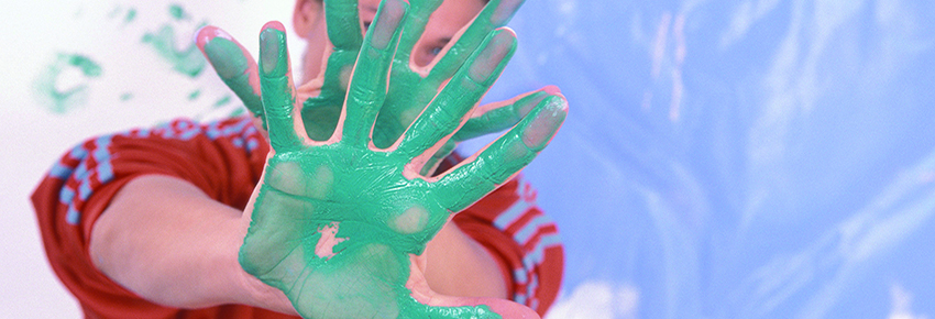 Frau verdeckt ihr Gesicht durch H&auml;nde, welche von einer t&uuml;rkisen Farbe bedeckt sind.