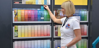 Frau steht vor einer gro&szlig;en Auswahl an verschiedenen Farbpaletten.
