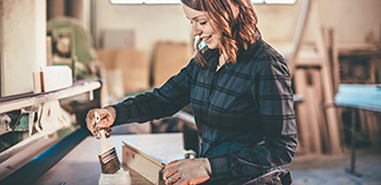 Frau streicht Holz in einer Farbe.