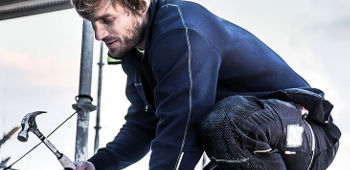 Mann arbeitet mit einem Hammer in einer Arbeitskleidung