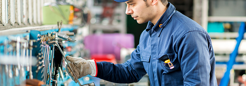 Mann arbeitet in einer Werkstatt und tr&auml;gt eine blaue Arbeitskleidung