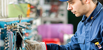 Mann arbeitet in einer Werkstatt und tr&auml;gt eine blaue Arbeitskleidung