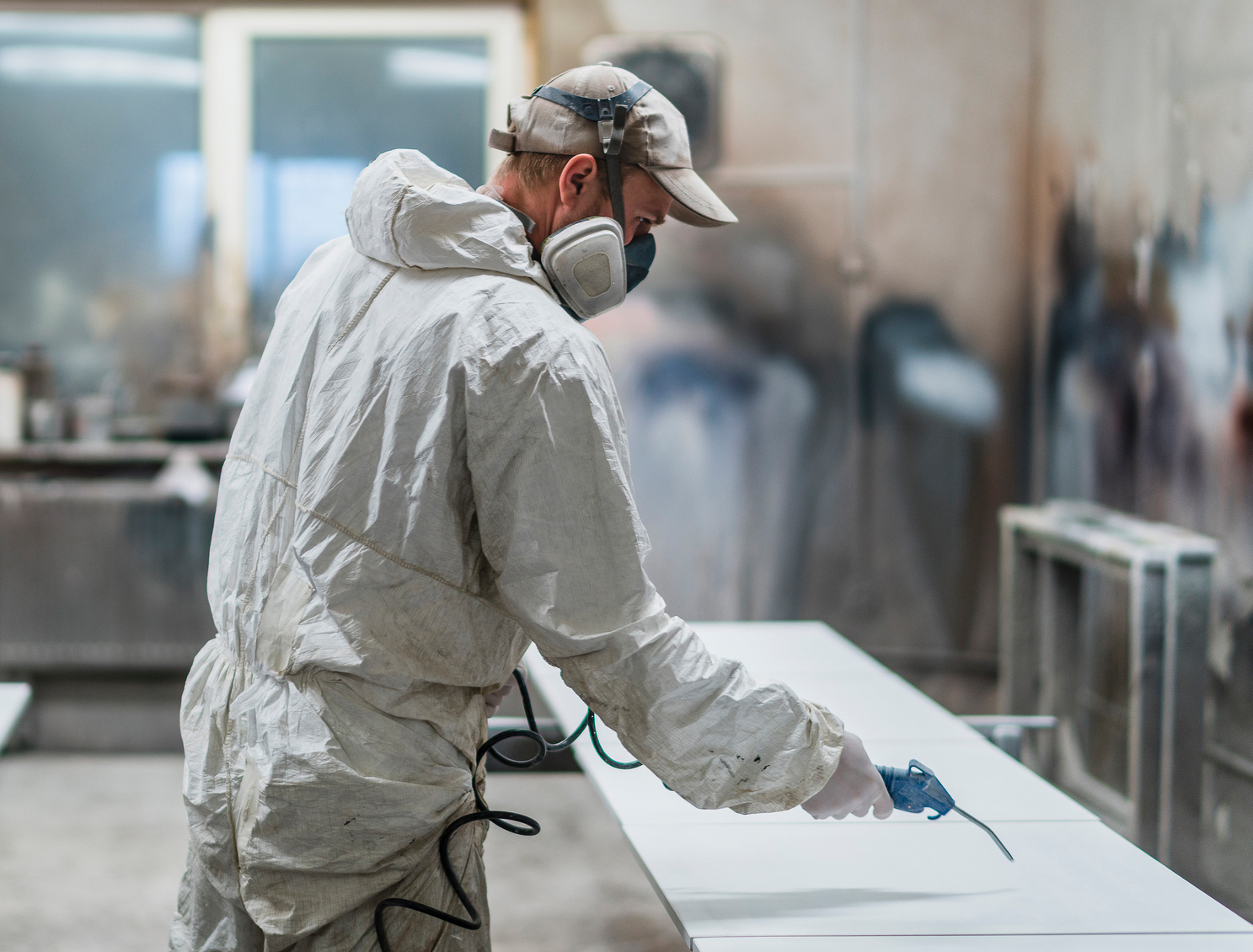 Mann, welcher eine Schutzkleidung und Atemmaske trägt, arbeitet mit einem Druckluftschlauch.