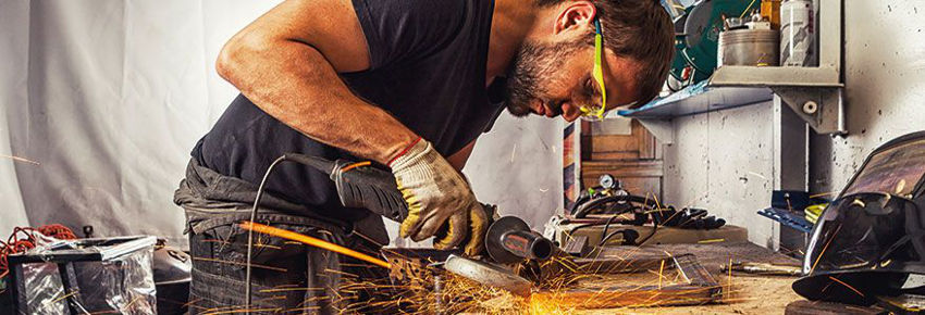 Mann, welcher eine Schutzbrille tr&auml;gt, arbeitet in der Werkstatt mit einem Winkelschleifer.