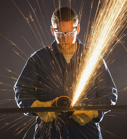 Mann mit Schutzkleidung arbeitet mit einem Winkelschleifer. Es sprühen Funken.